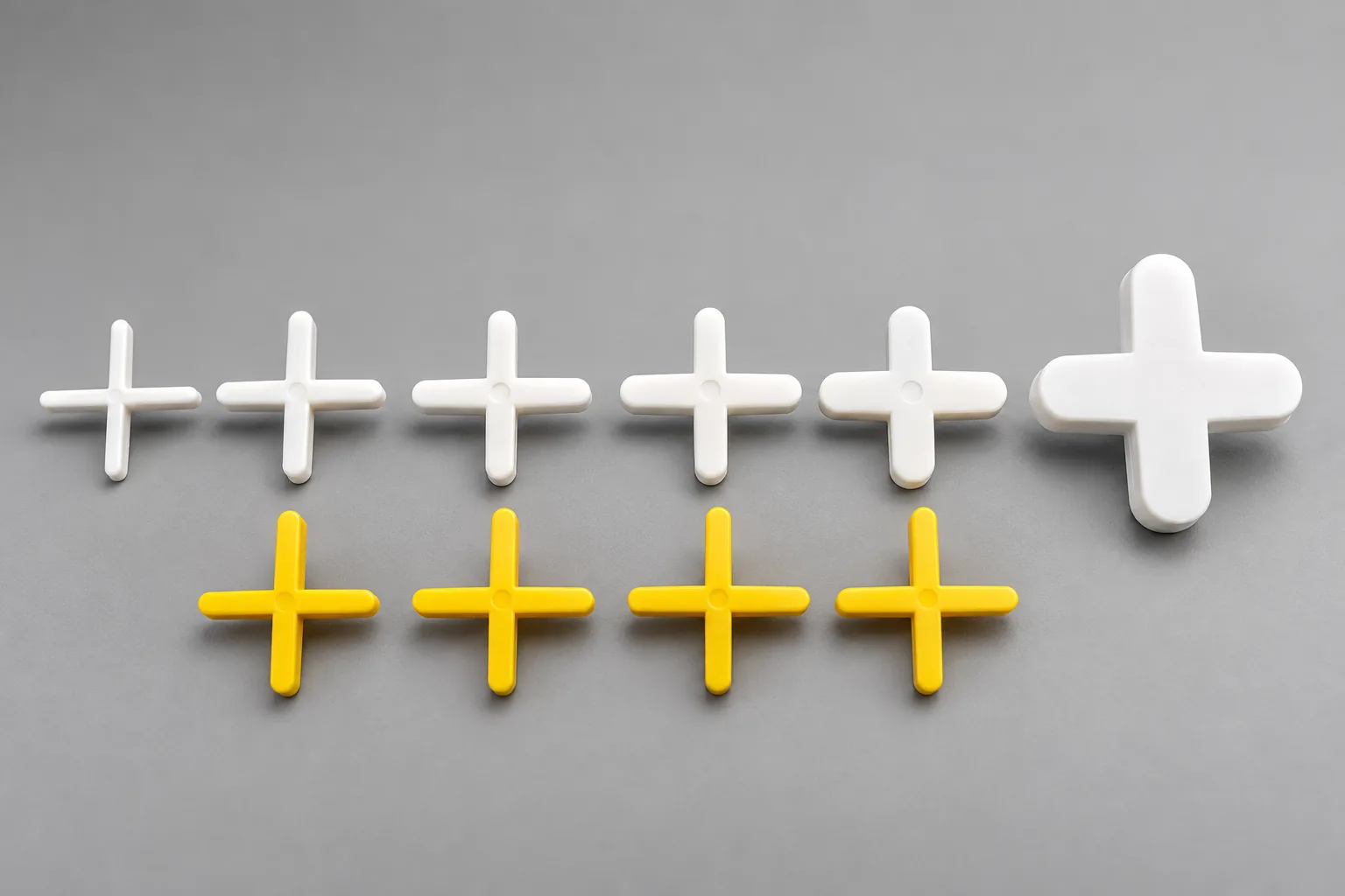 White and yellow cross tile spacers in several sizes on a gray surface